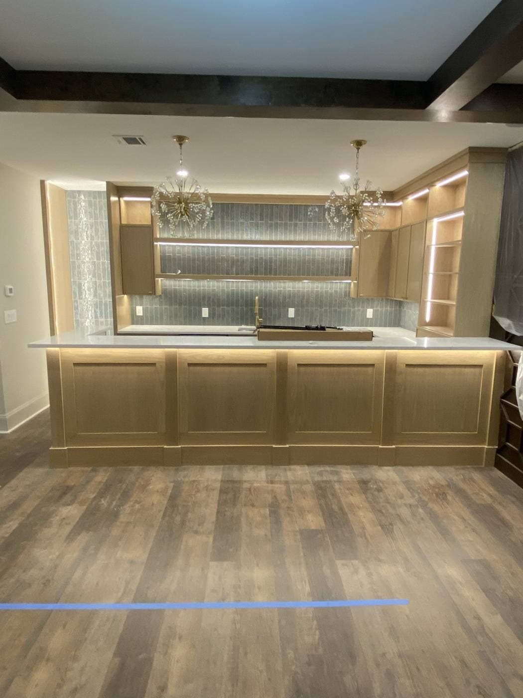 A light oak bar with two glass chandeliers, a tiled backsplash, and open shelving lit from within.