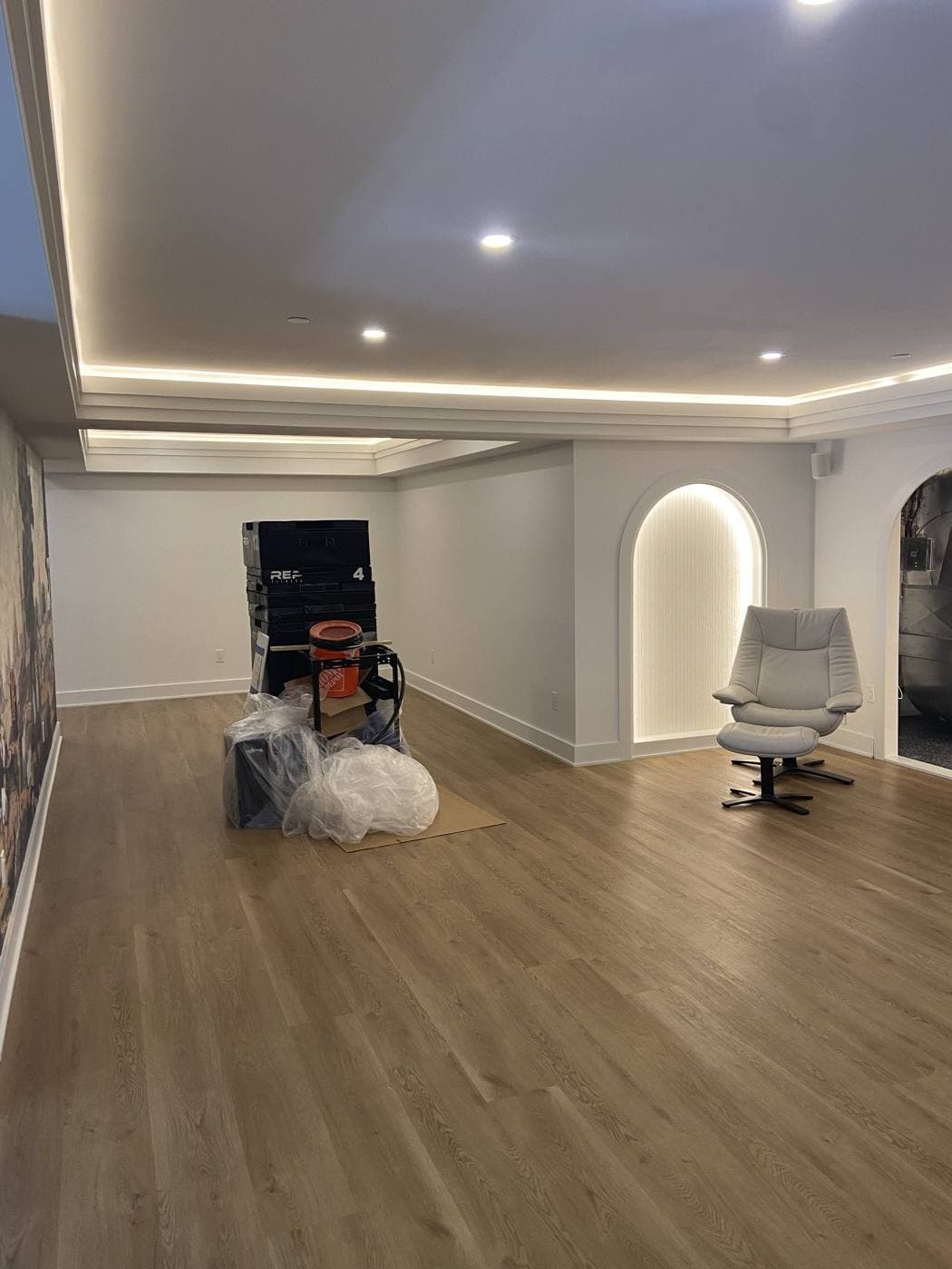 A finished lower level with warm cove lighting around a stepped ceiling and a softly lit arched wall niche.