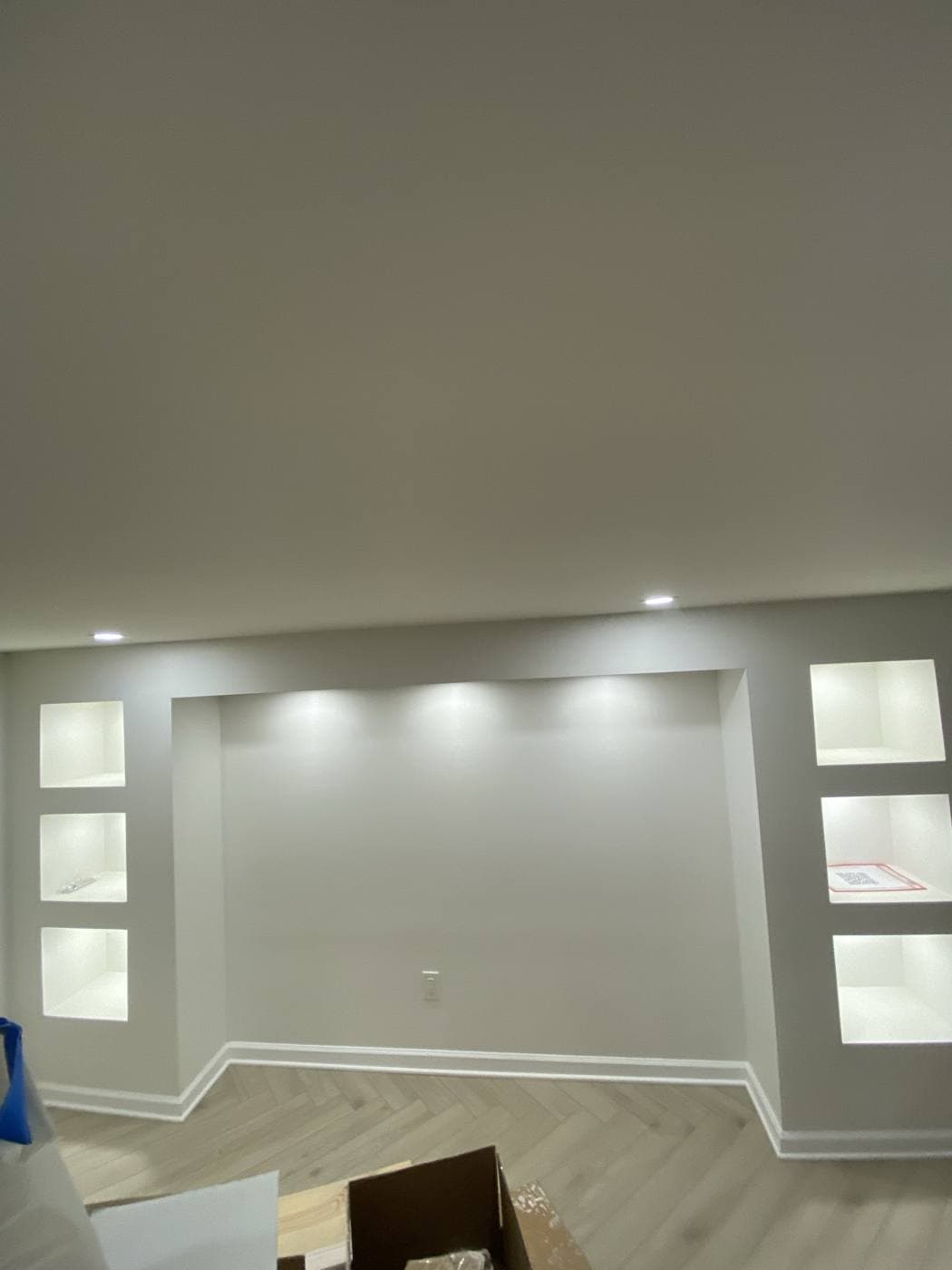 A wall with two columns of recessed display niches, each lit from within, beside a wall-washed alcove.