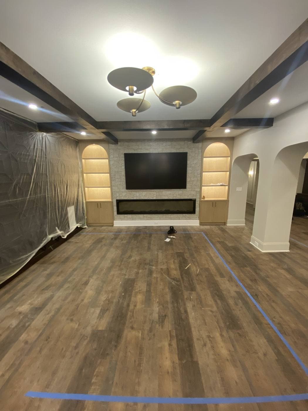 A living space with exposed beams, a linear fireplace and TV in a stone surround, flanked by two lit arched niches.