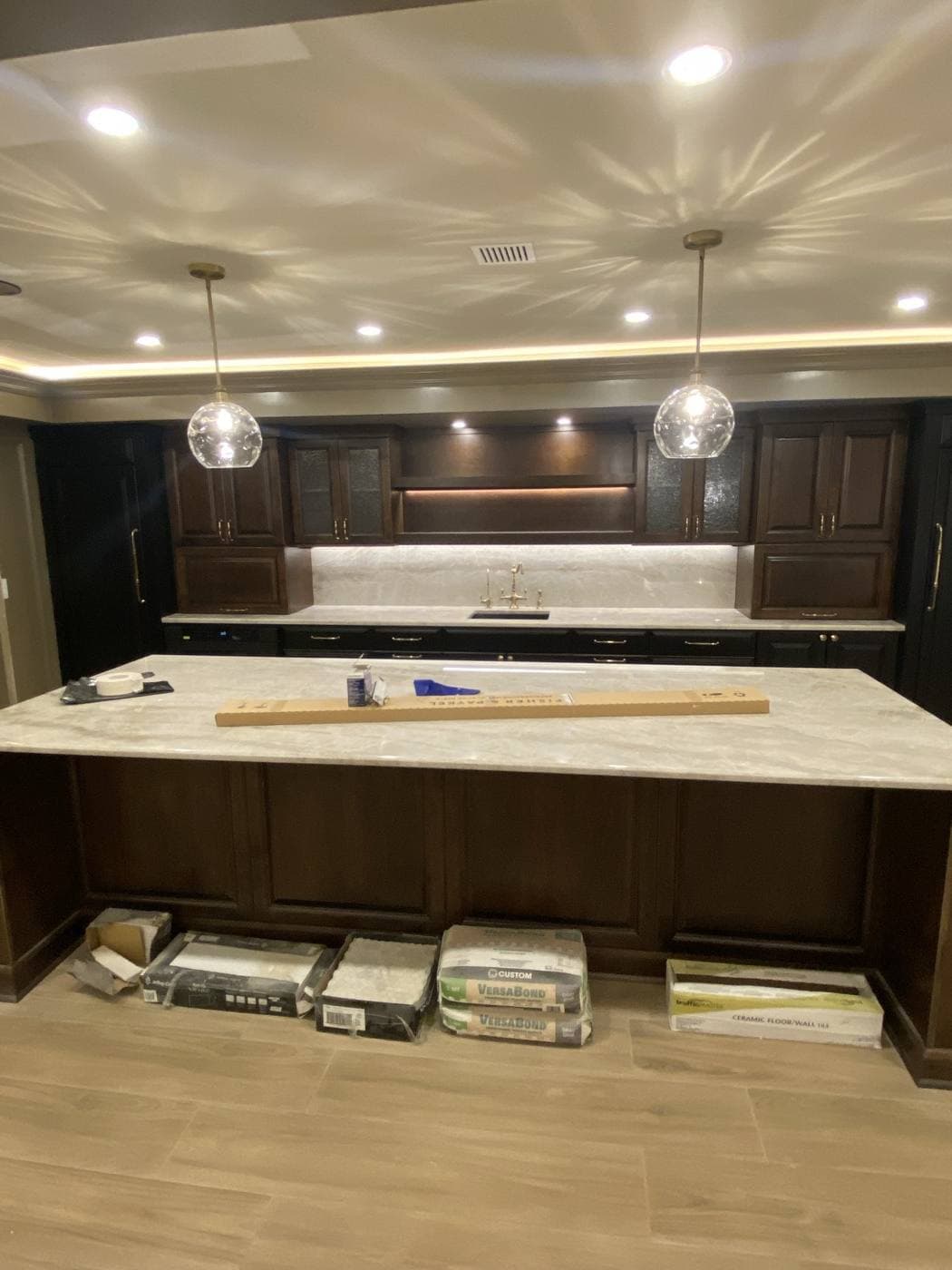 A kitchen with dark cabinetry, two glass pendants over a stone island, under-cabinet lighting, and cove lighting around the ceiling.