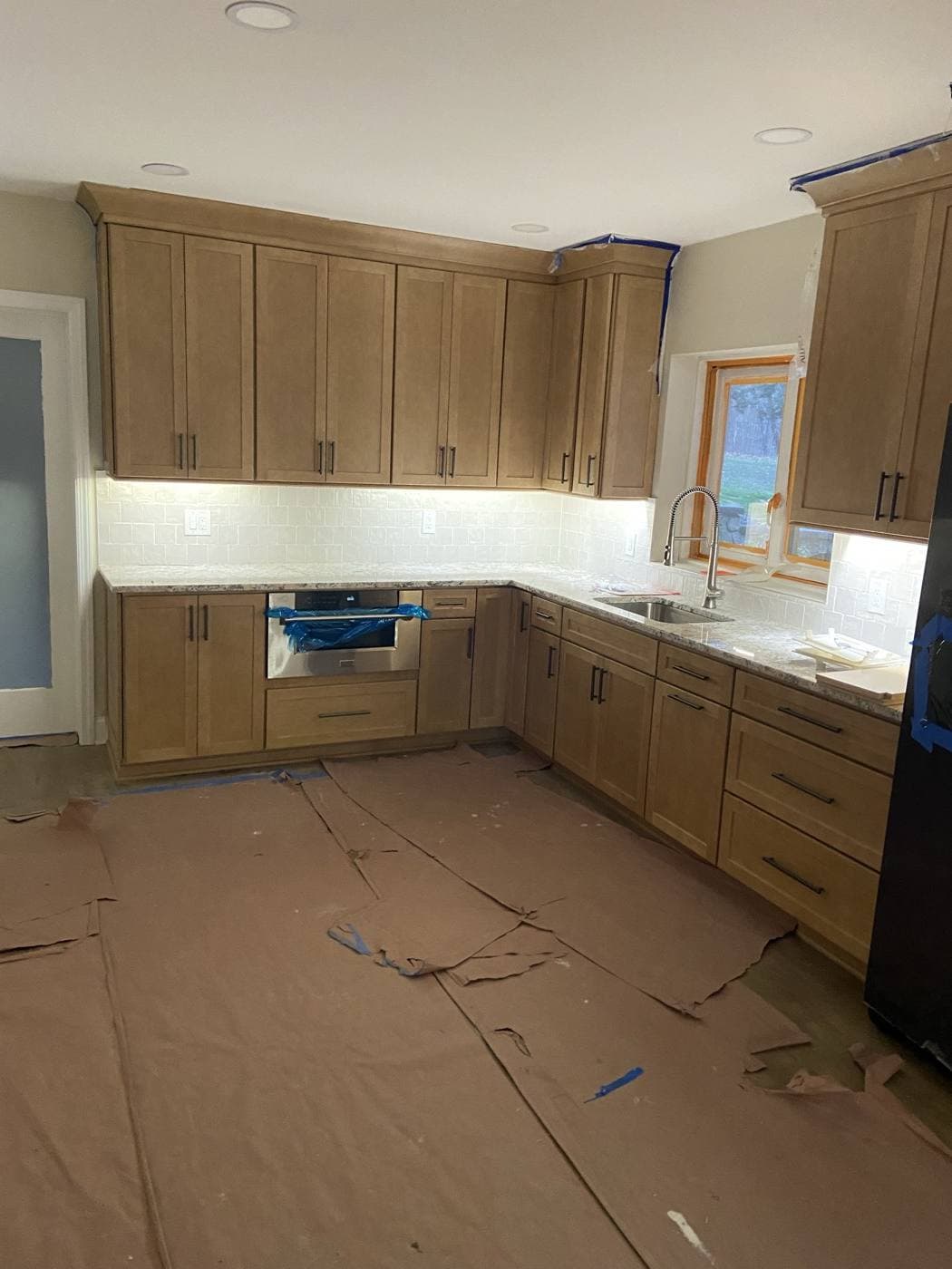 A kitchen mid-project with under-cabinet lighting on and the floor fully covered in protective drop cloths.