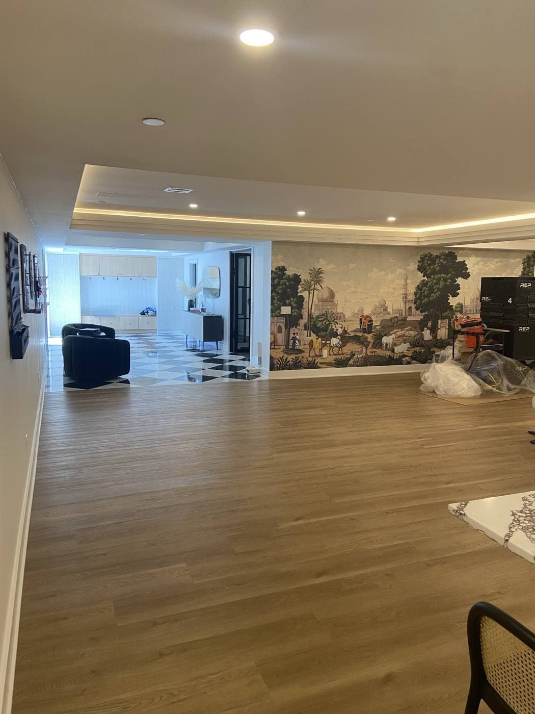 A large finished lower level with cove lighting around a dropped ceiling and recessed cans over a mural wall.