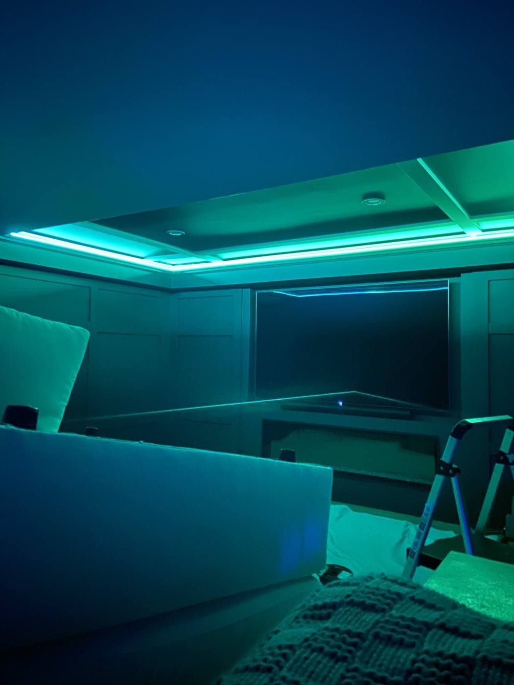 A media room with panelled walls lit in teal by cove lighting around a coffered ceiling.