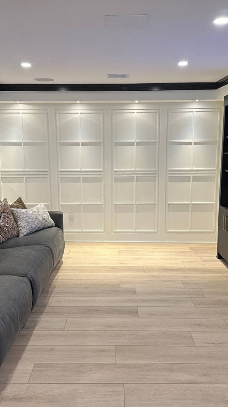 A white panelled accent wall evenly lit from above by a row of recessed wall-wash fixtures.