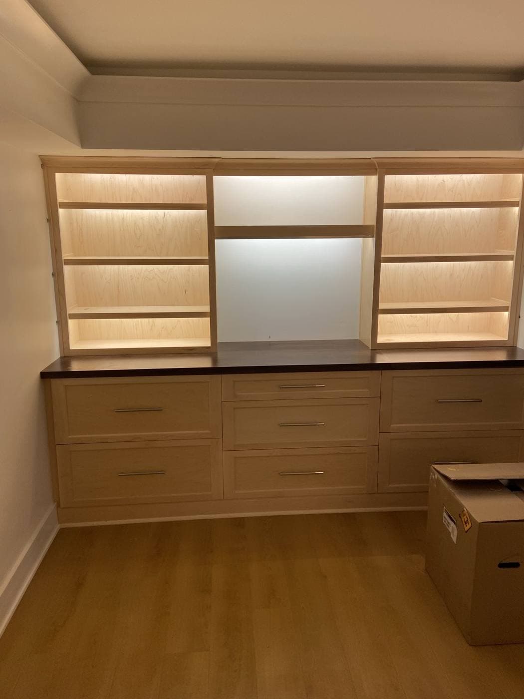 A maple built-in with three bays of shelving, each shelf lit from concealed LED strips.