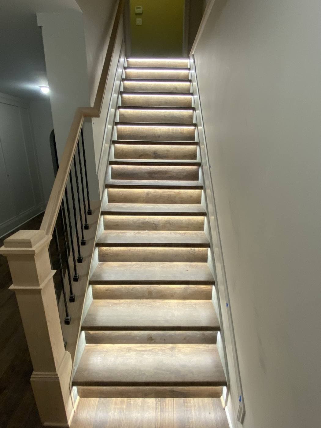 A staircase where each tread is lit from a concealed LED strip beneath its nosing, washing light down the riser below.