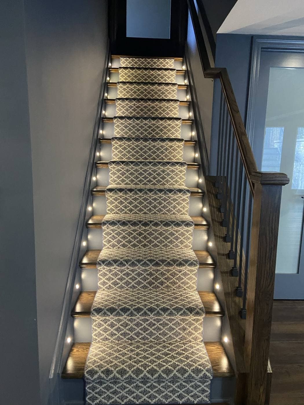 A staircase with a patterned runner, lit by small recessed lights in the side walls at every tread.