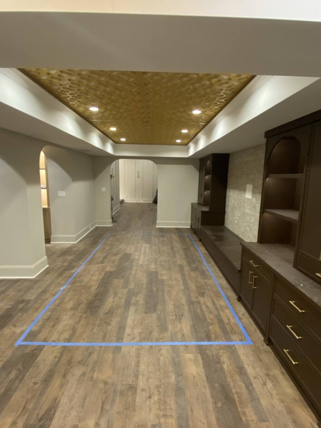 A hallway with a gold textured ceiling panel framed by cove lighting and recessed cans.