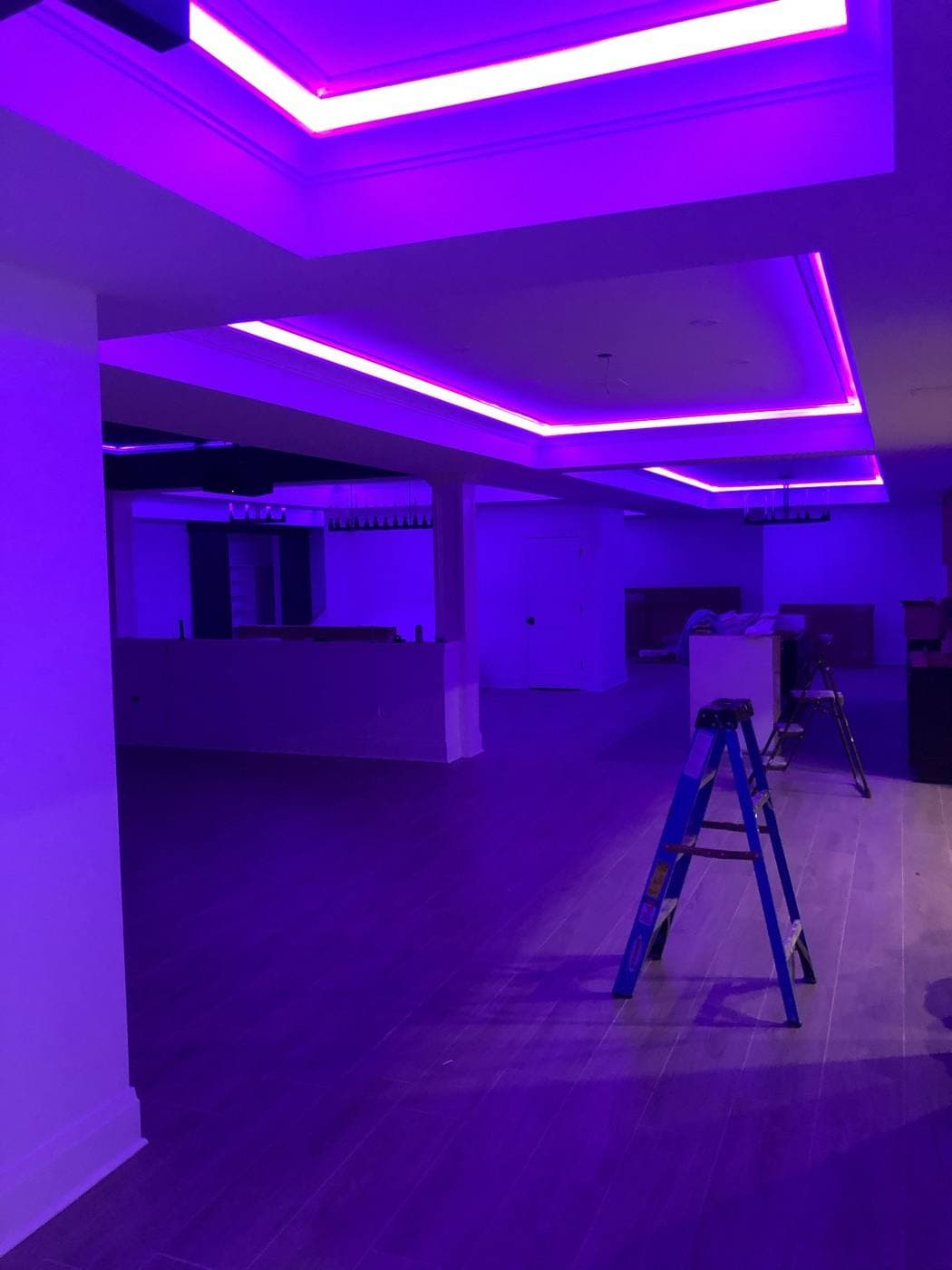 A large open room lit entirely in purple by concealed LED strips running around three stepped tray ceilings.