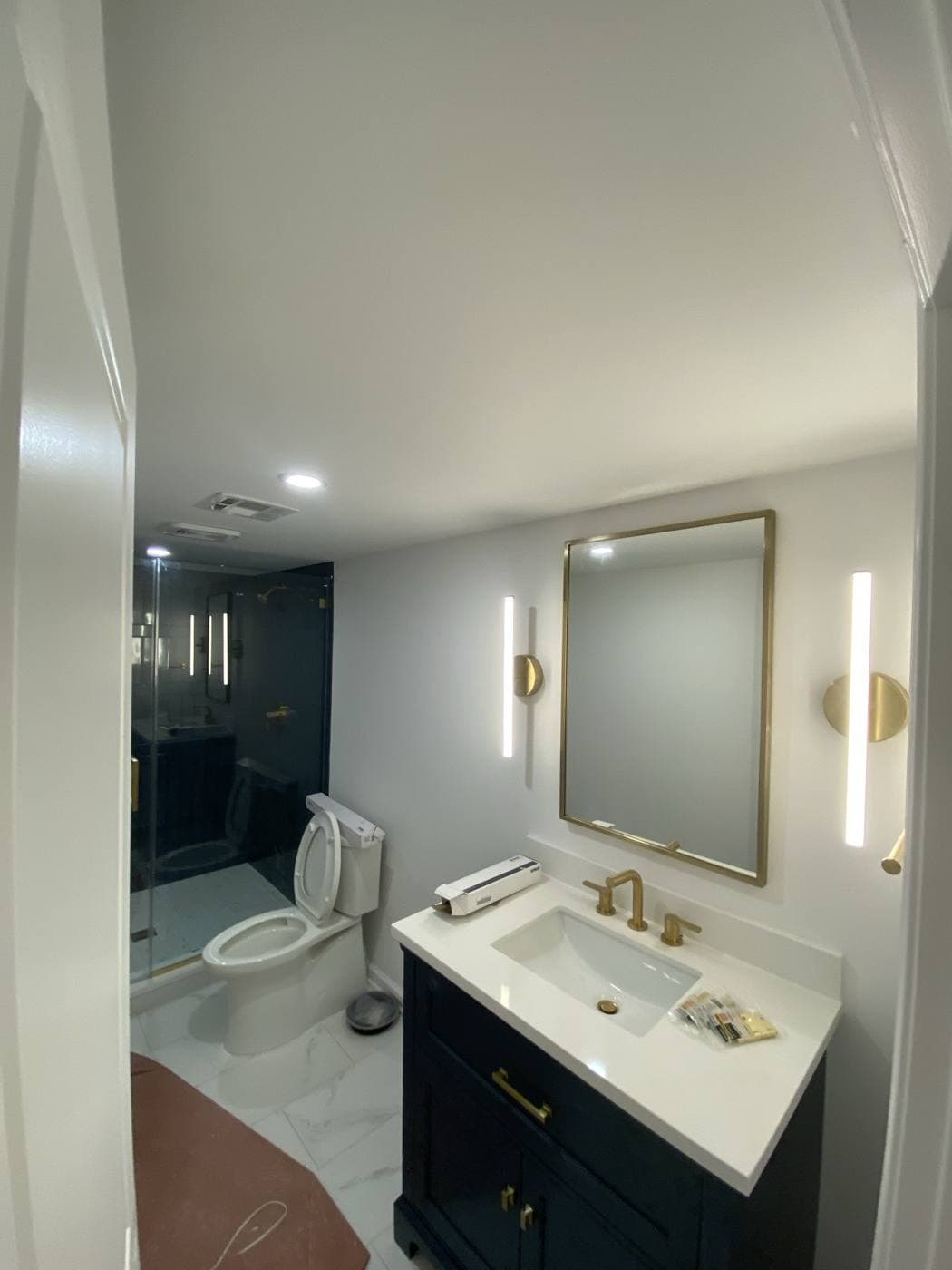 A bathroom vanity with a brass-framed mirror between two vertical linear sconces, and recessed lighting overhead.